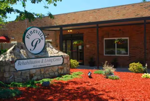 Exterior view of Pineville Rehabilitation and Living Center entrance with a stone sign and landscaping.