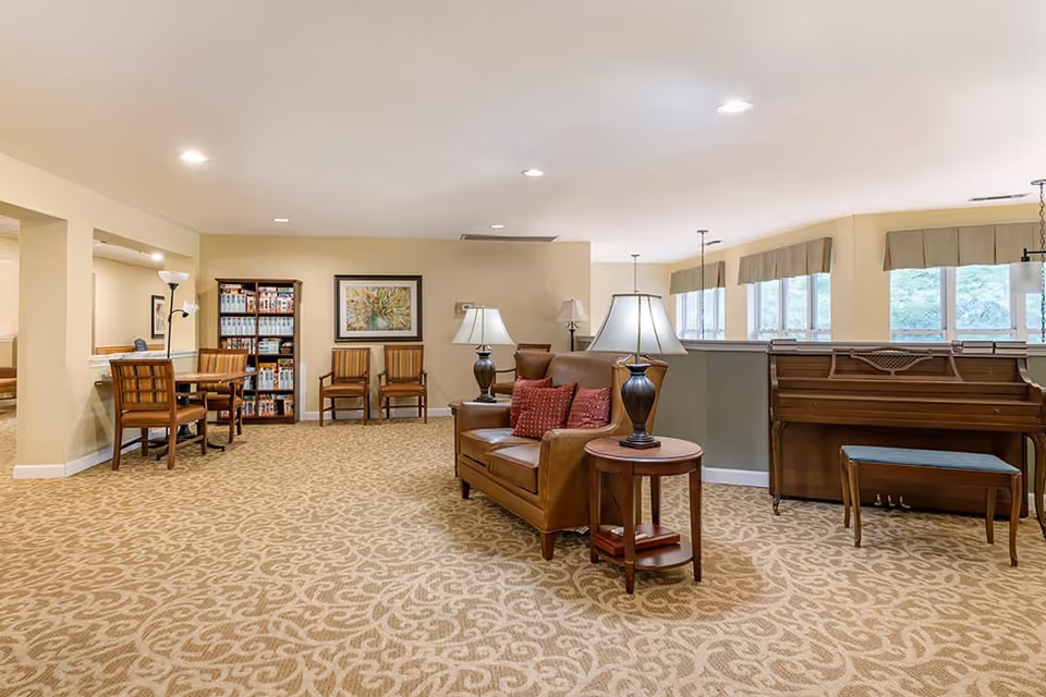 Comfortable common lounge with a leather sofa, side tables and lamps, a dining table and chairs, bookshelf, and a piano.