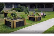 Outdoor lawn area with raised garden beds, a sidewalk, and benches near Twin Maples Healthcare.