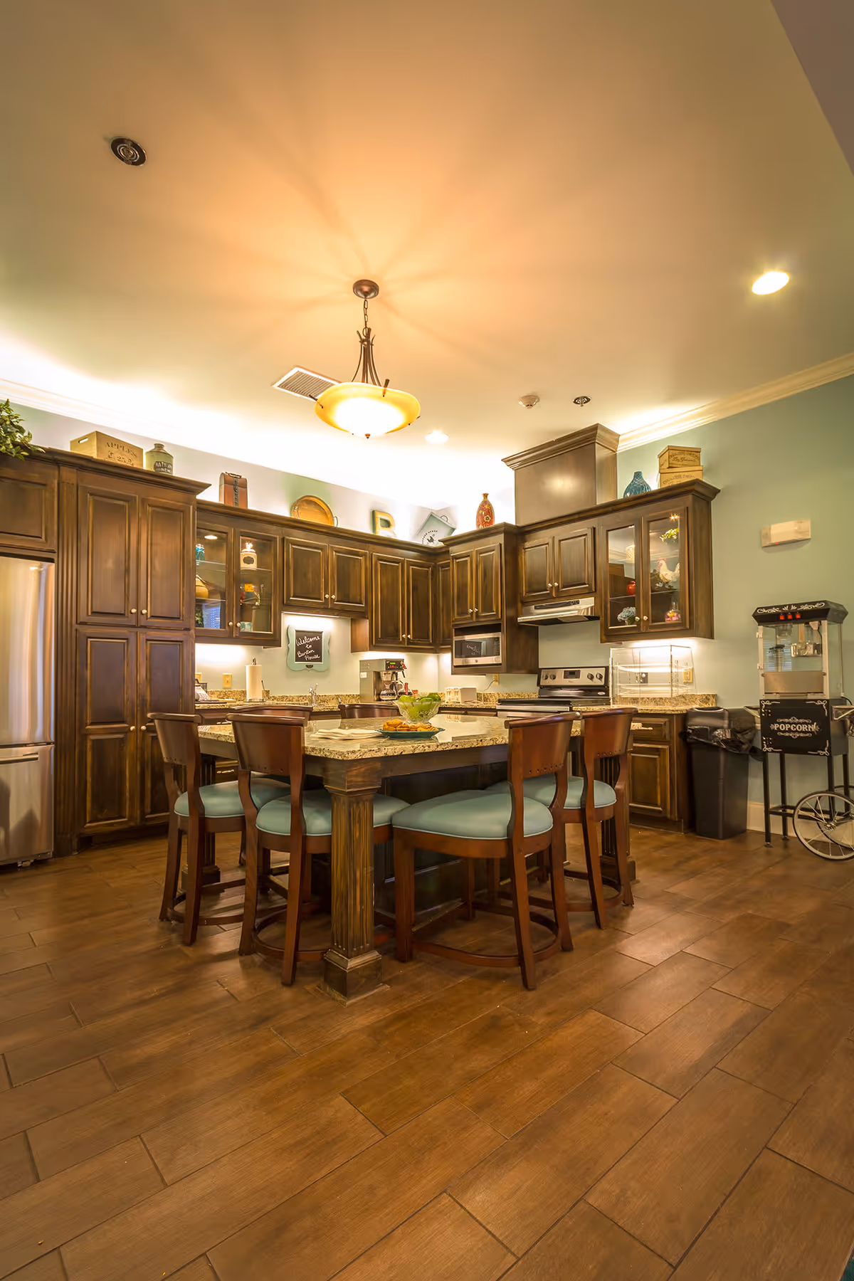 Spacious kitchen with a central island surrounded by stools, dark wooden cabinets, stainless appliances, and overhead lighting.