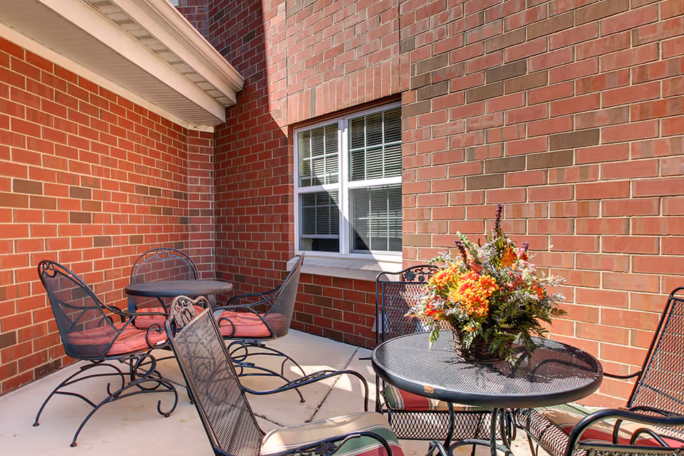 Small outdoor brick courtyard with metal patio tables and chairs, one table holding a colorful flower arrangement.