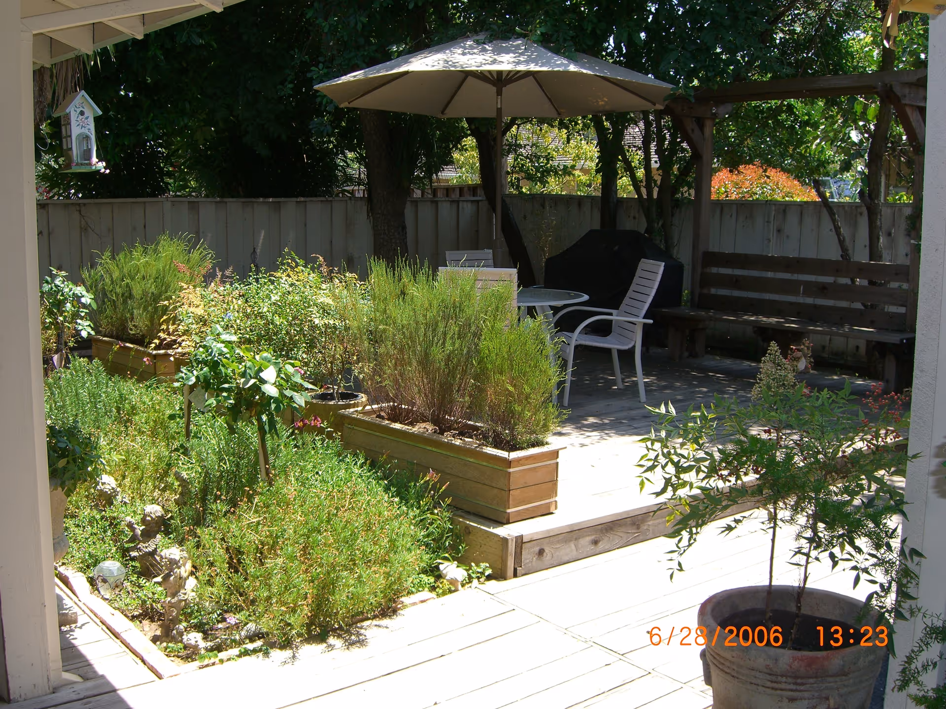 Shaded backyard patio with raised planter boxes, a table and chairs under a large umbrella and potted plants.