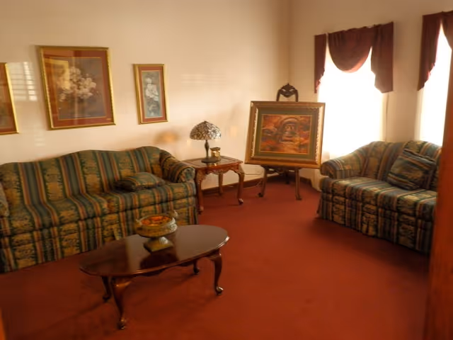 A cozy living room with patterned sofas, paintings, coffee table, and red carpet.