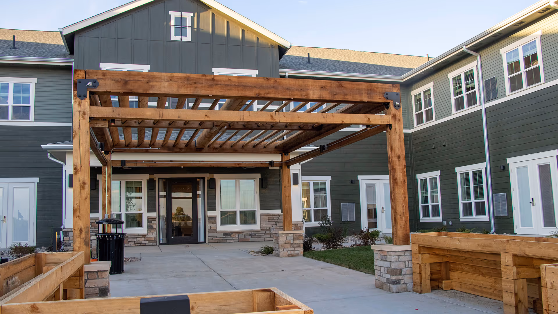 Exterior courtyard and main entrance of a two-story building featuring a large wooden pergola.