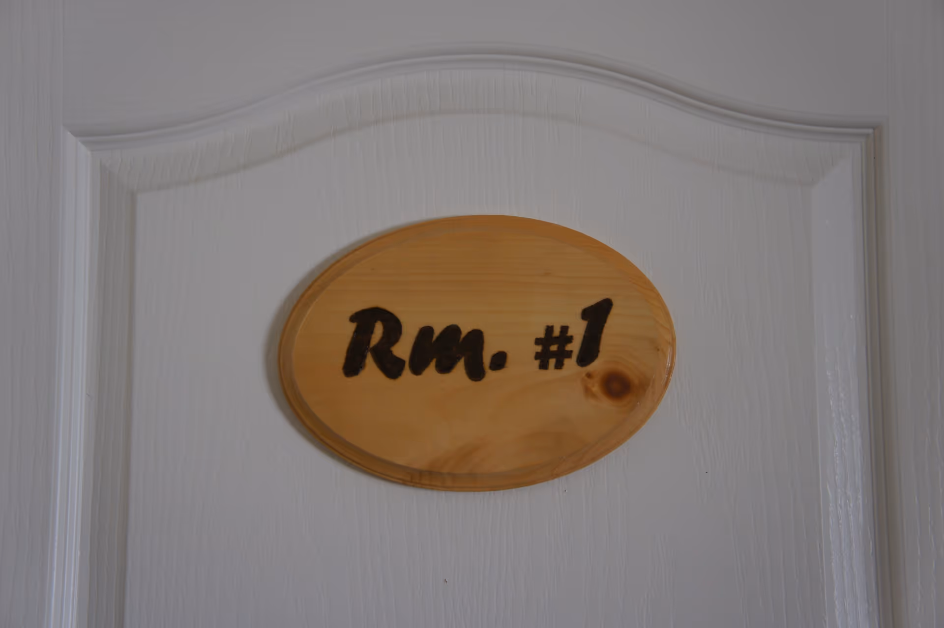 White paneled door with a wooden oval plaque that reads "Rm. #1".