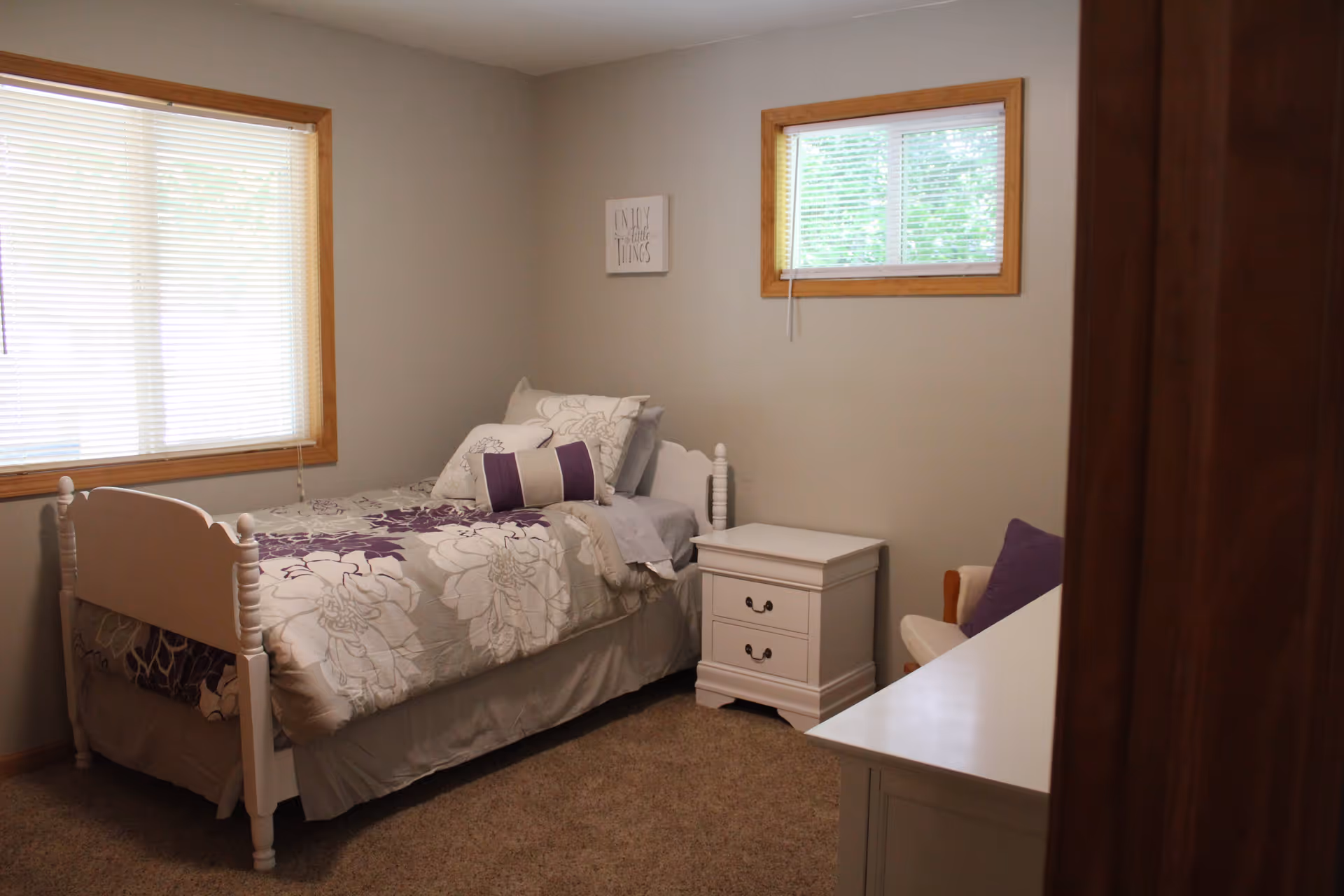 Small bedroom with a twin bed, nightstand, dresser, chair, and two windows.