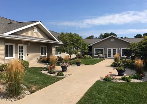 Courtyard walkway bordered by grass, potted plants, and single-story beige buildings under a blue sky.