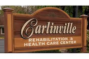 Wooden sign reads Carlinville Rehabilitation & Health Care Center in front of trees.