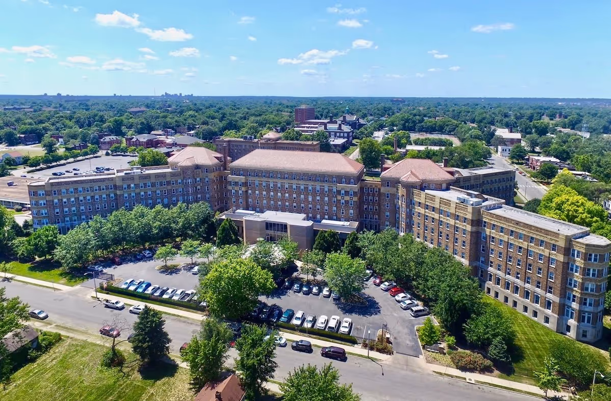Aerial view of a large senior apartment complex named Homer G Phillips Senior Apartments surrounded by trees and parking lots under a blue sky with scattered clouds.