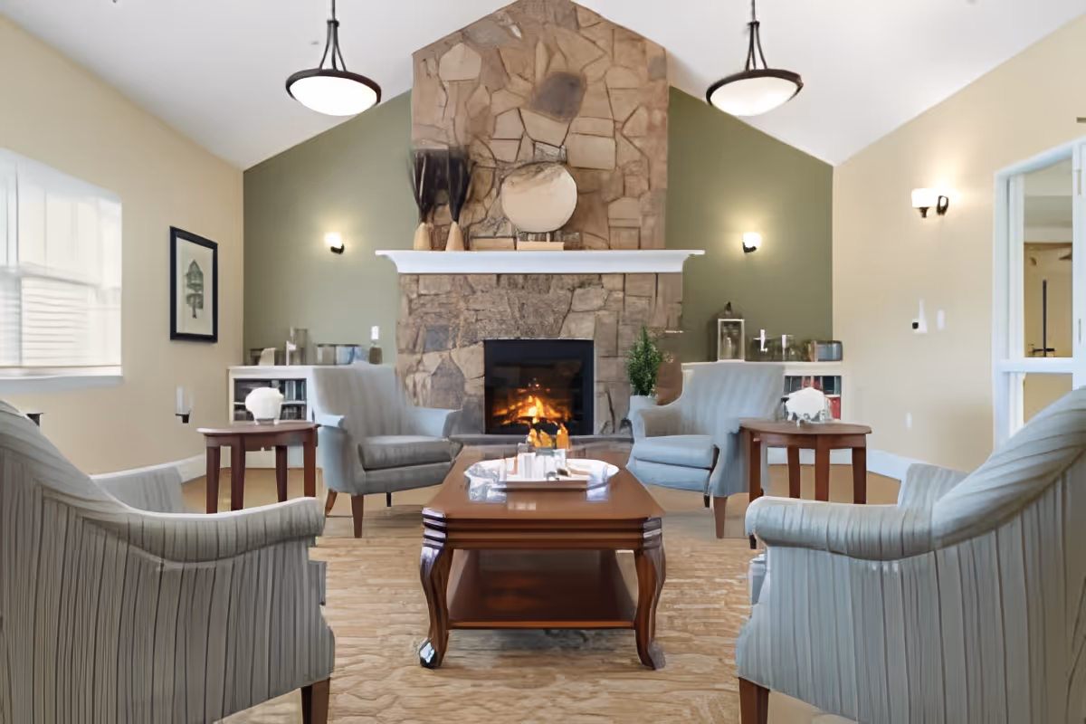 Cozy common room with armchairs and a coffee table arranged around a stone fireplace.