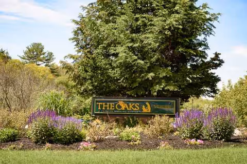 Outdoor view of The Oaks sign amid shrubs and colorful flowers.