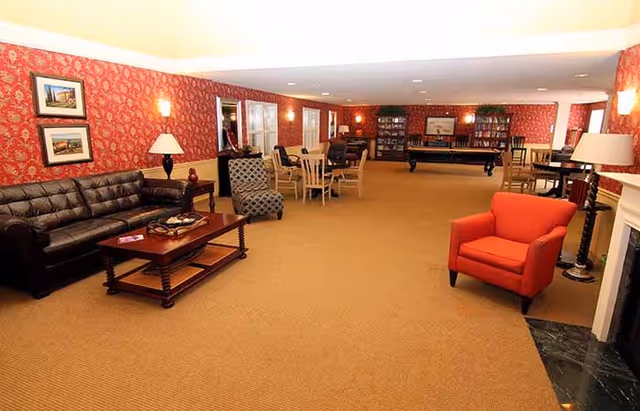 Spacious furnished community lounge with sofas, chairs, tables, bookshelves and a pool table, decorated with red patterned wallpaper.