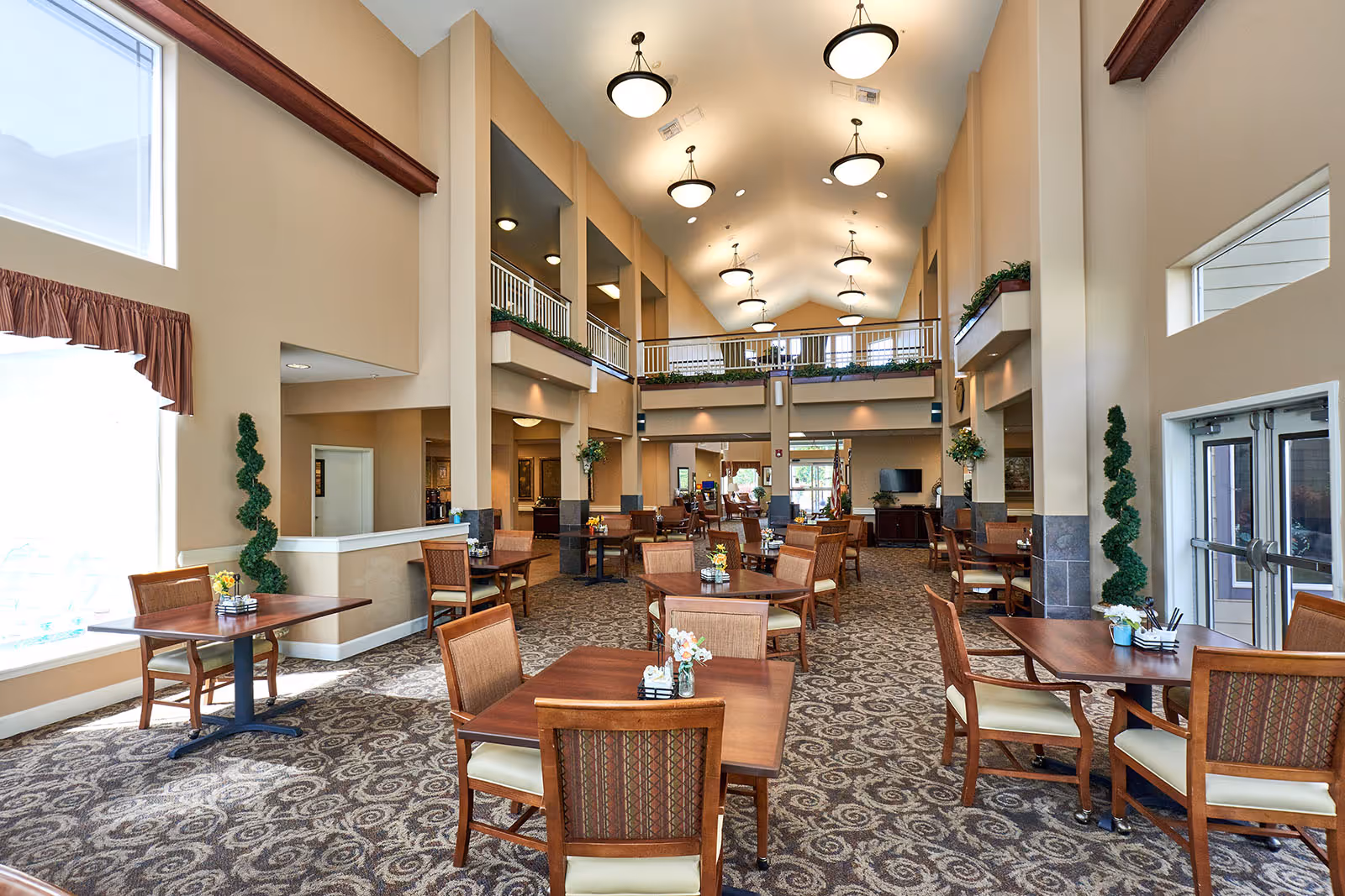 Spacious two-story communal dining area with multiple wooden tables and chairs, high ceilings, and a second-floor balcony overlooking the seating.