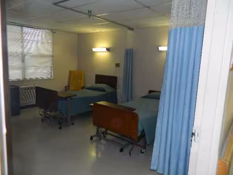 Hospital-like patient care room with two beds, blue privacy curtains, and a window.