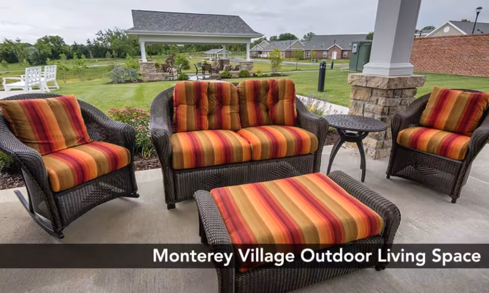 Outdoor covered patio with wicker seating and striped cushions facing a lawn and pavilion.
