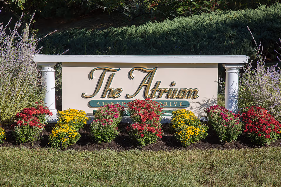 A landscaped sign for The Atrium at Veronica Drive, surrounded by colorful flowers and greenery.
