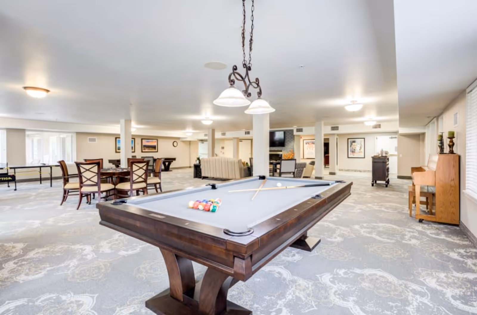Spacious senior living community recreation room with a pool table in the foreground, seating areas, and a piano.