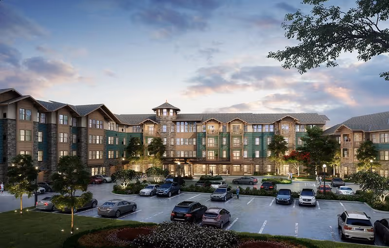 Front view of a multi-story senior living building with landscaped grounds and a parking lot filled with cars at dusk.