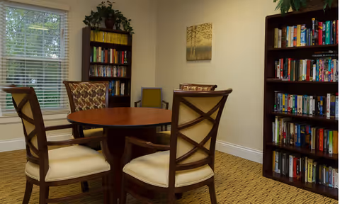 Cozy interior room with a round wooden table surrounded by four chairs and bookshelves filled with books.