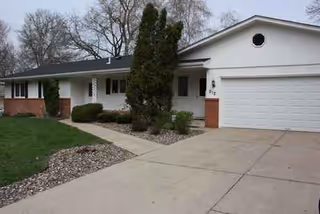 A single-story house with a white garage door and landscaped front yard.