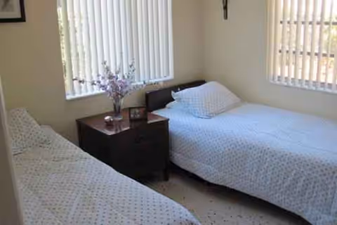 Two single beds with white polka-dot sheets, a dark nightstand, and windows with blinds.