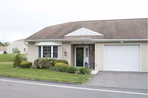 Single-story residential building with a front door, window, garage, and manicured landscaping.