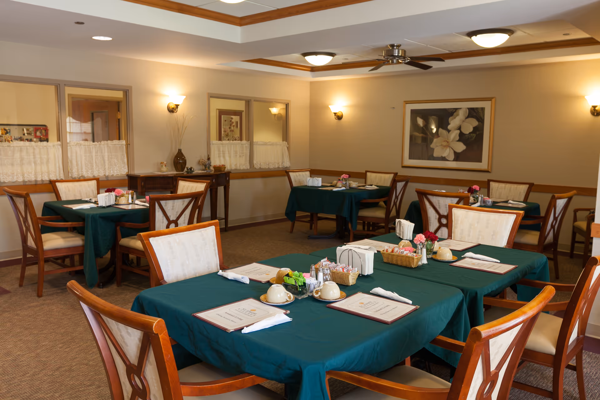 Dining room with multiple tables covered in green tablecloths, set with menus, condiments, and chairs.