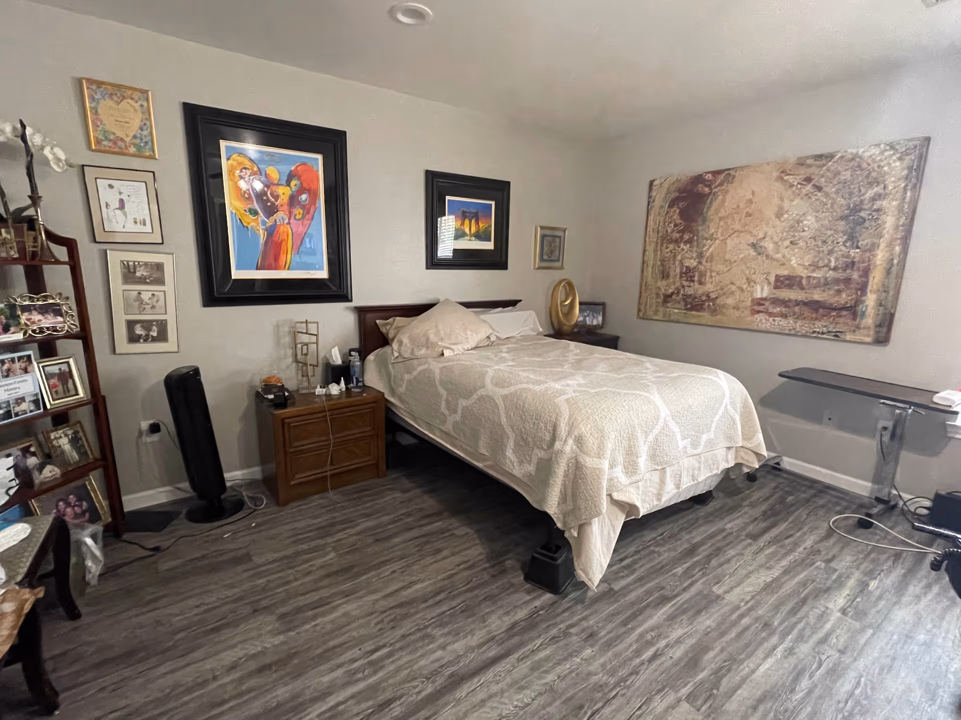 Neatly furnished bedroom with a bed, nightstands, multiple framed artworks on the walls, and wood-look flooring.