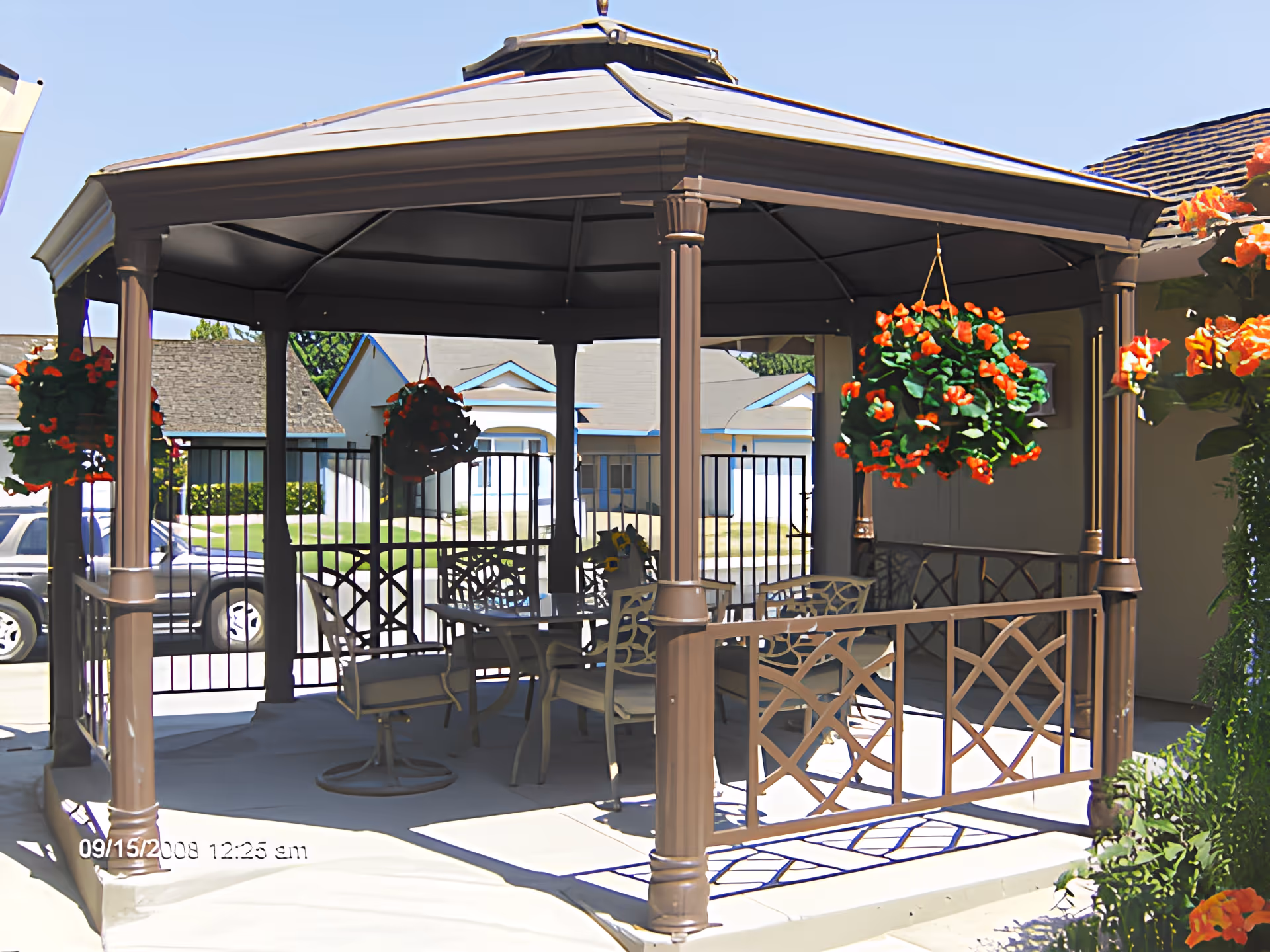 A covered outdoor gazebo on a patio with a dining table, chairs, and hanging flower baskets.