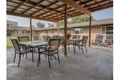 Covered outdoor patio with tables and chairs under a wooden pergola in a courtyard.