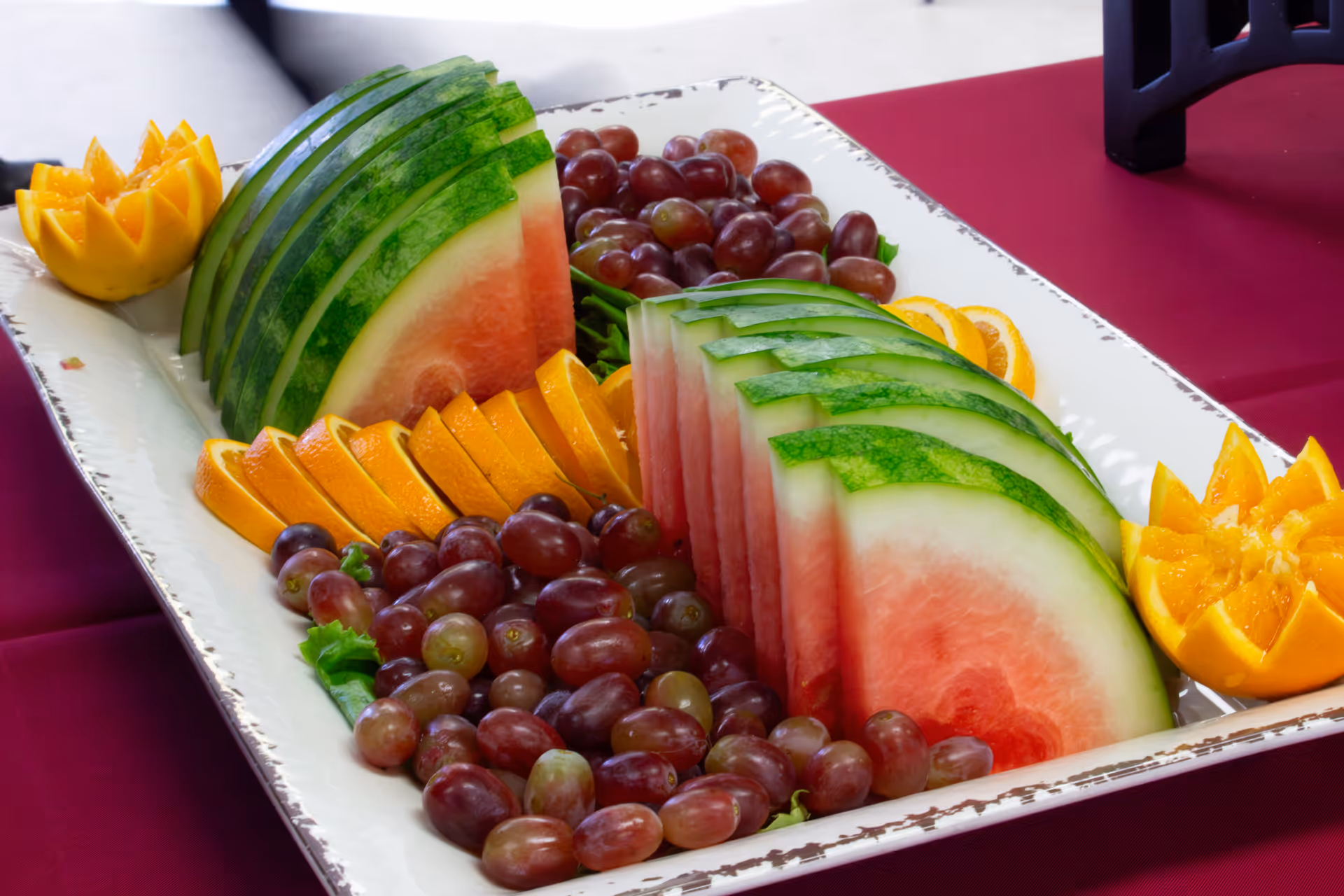 A platter of sliced watermelon, red grapes, and orange wedges arranged on a white serving tray.