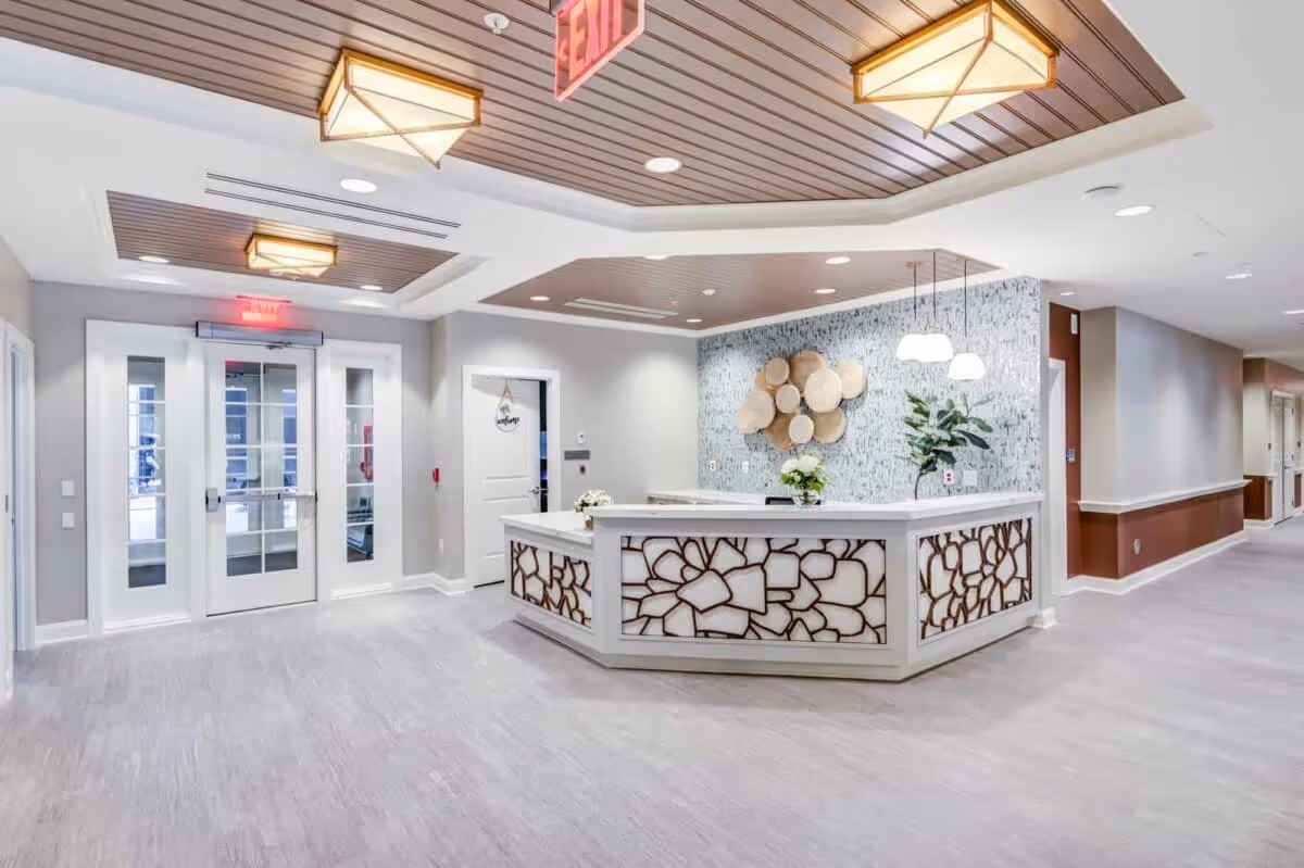 A bright and modern reception area inside Queenstown Landing facility featuring a white reception desk with decorative paneling, a textured accent wall with circular wall art, pendant lights hanging above the desk, and a double glass door exit with illuminated exit signs.