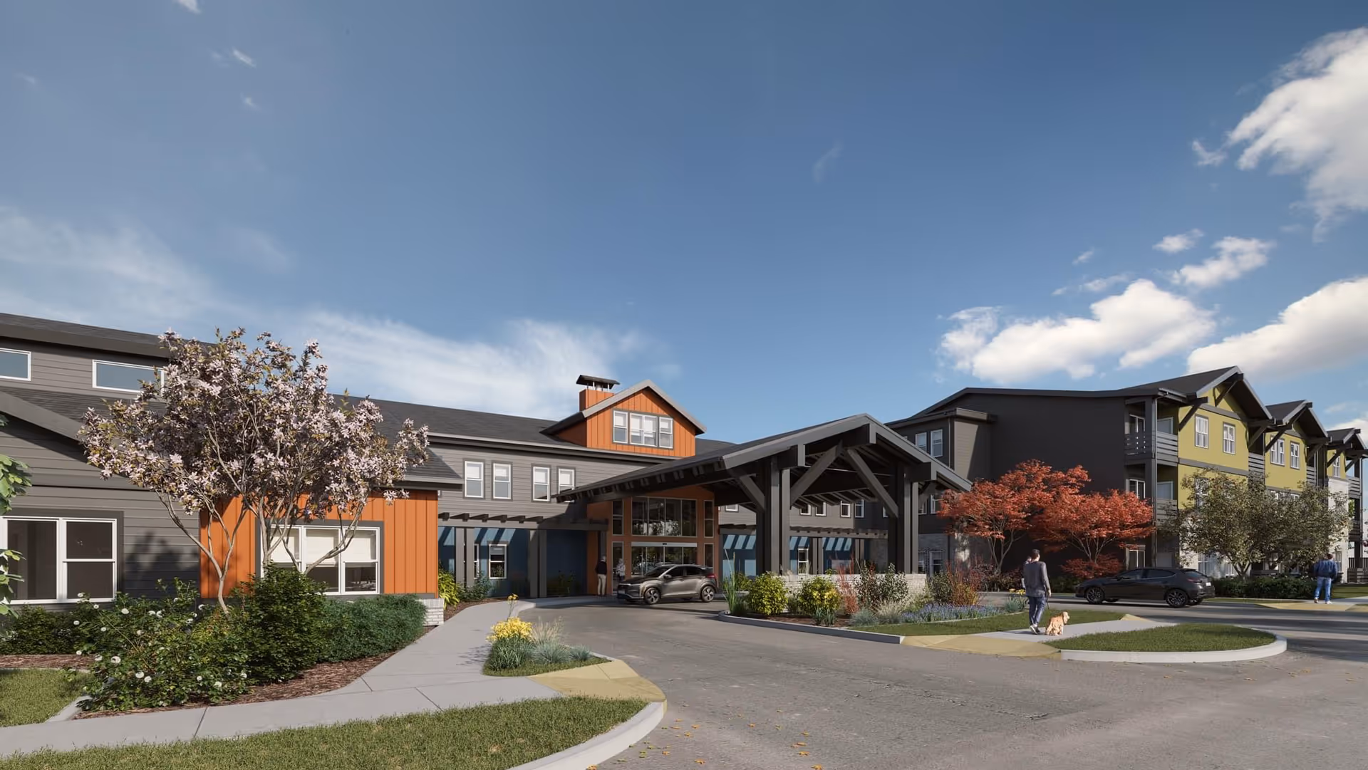 Exterior view of The Pointe at Meridian senior living facility showing a modern multi-story building with a covered entrance, landscaped greenery, trees with autumn foliage, and a person walking a dog on the driveway under a partly cloudy sky.