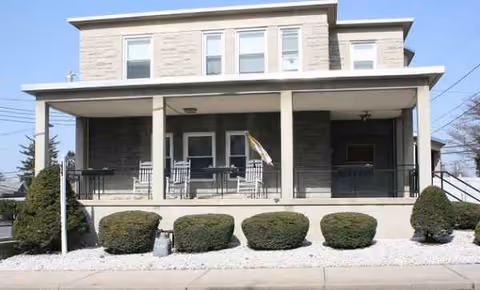 Two-story stone retirement home with a covered front porch and neatly trimmed shrubs.