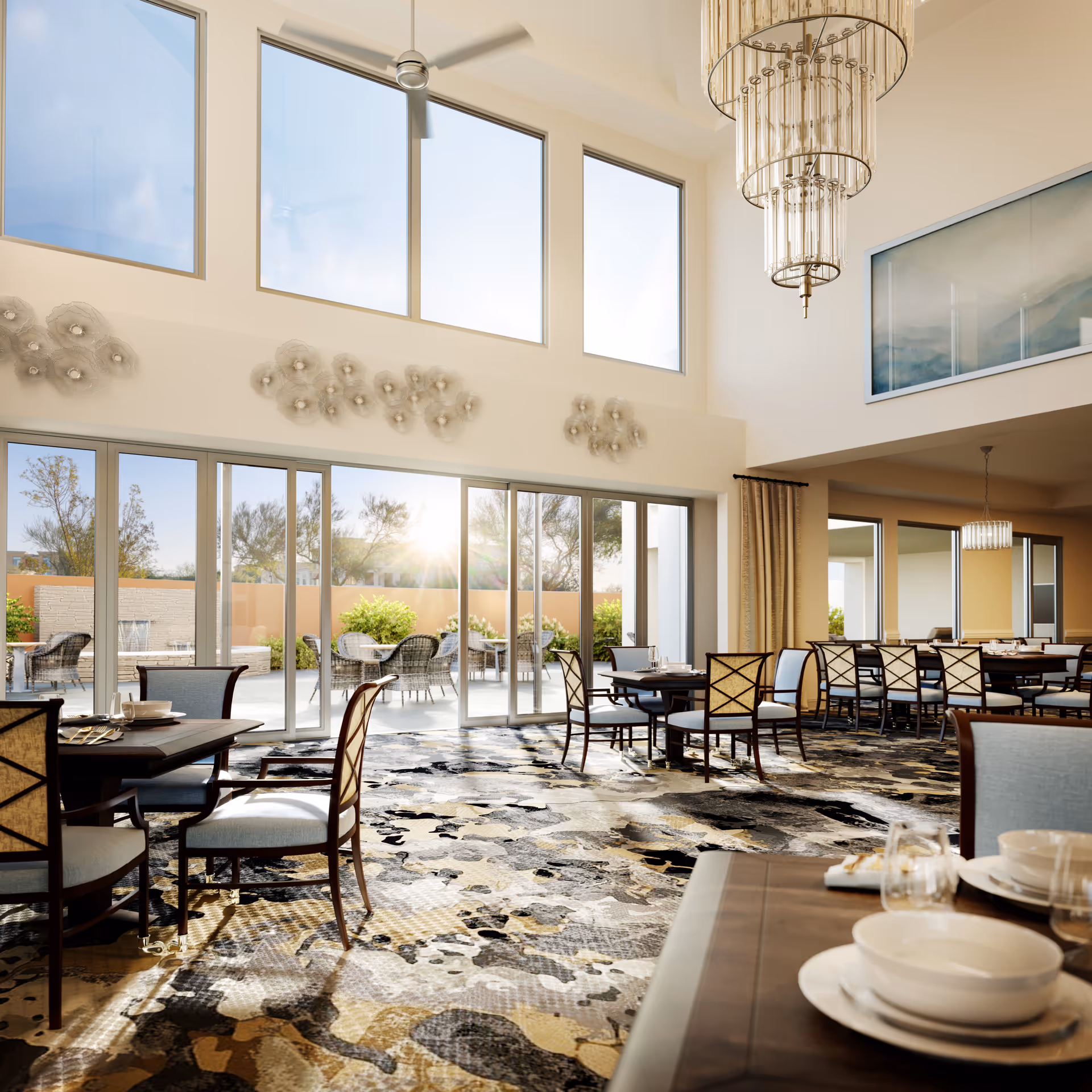 Sunlit elegant dining room with multiple tables and chairs, high ceilings, large windows and sliding glass doors to an outdoor patio.
