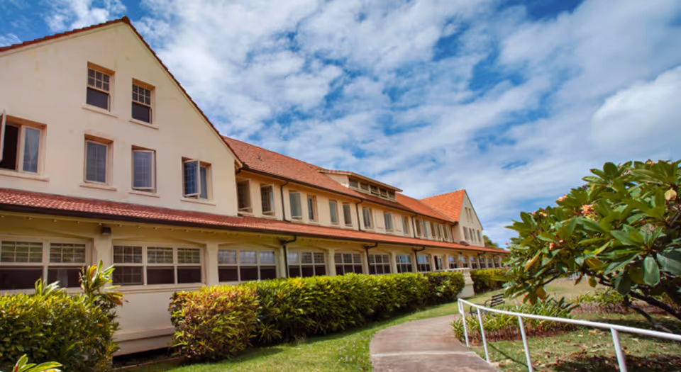 Exterior view of a beige senior living building with red roof and manicured walkway.
