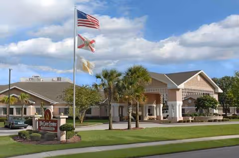 Senior living facility exterior with flags, palm trees and a front entrance.