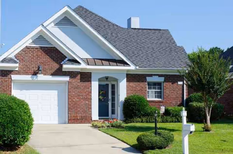 Front view of a brick residential-style building with driveway, garage, and manicured lawn.