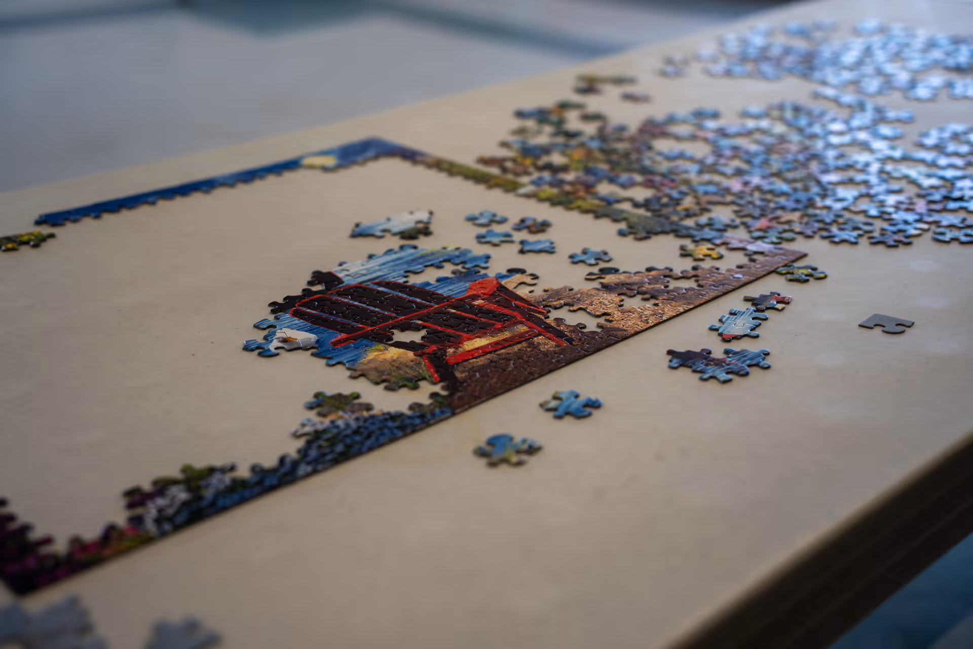 A partially completed jigsaw puzzle on a beige table, showing a red chair and some outdoor scenery with scattered puzzle pieces around it.