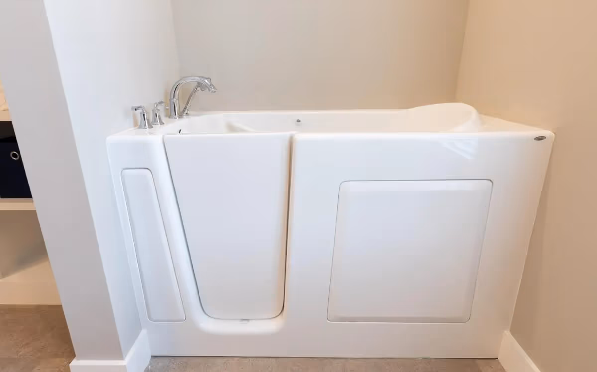 A white walk-in bathtub with a door, chrome faucet, and handles, installed in a bathroom corner with beige walls and a tiled floor.