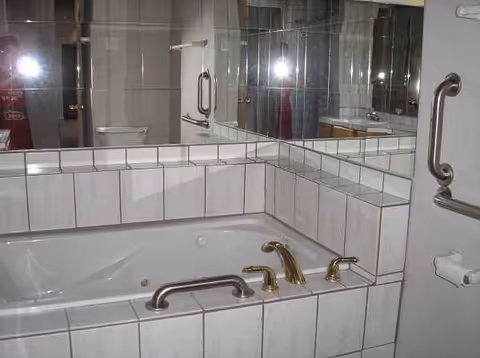 Tile-surrounded bathroom featuring a large tub, dual brass faucets, and safety grab bars.