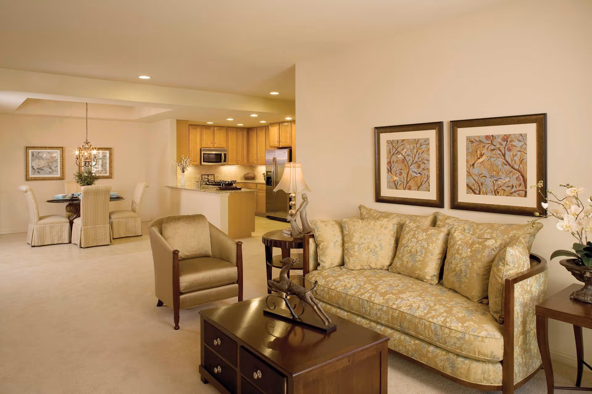 Open-concept living room with a patterned sofa, armchair, coffee table, and a view into the dining area and kitchen.