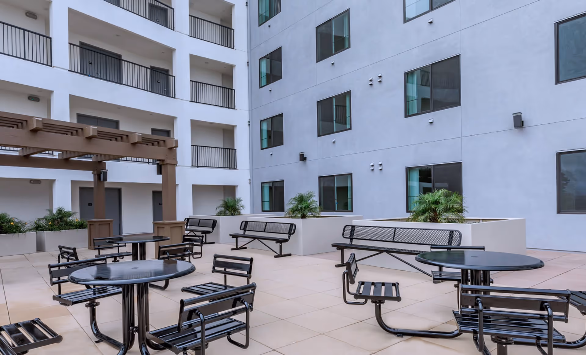 Courtyard patio with metal tables, chairs and benches surrounded by a multi-story apartment building and balconies.