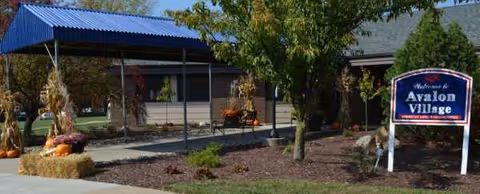 Front exterior of Avalon Village with blue canopy, sign, trees, and bench.