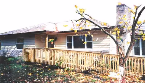 Exterior view of Esther's Place senior living facility with a wooden deck and autumn leaves.