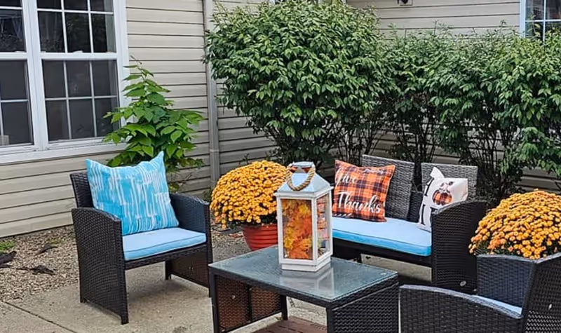 Outdoor seating area with wicker chairs, blue cushions, pumpkins, and lantern centerpiece.