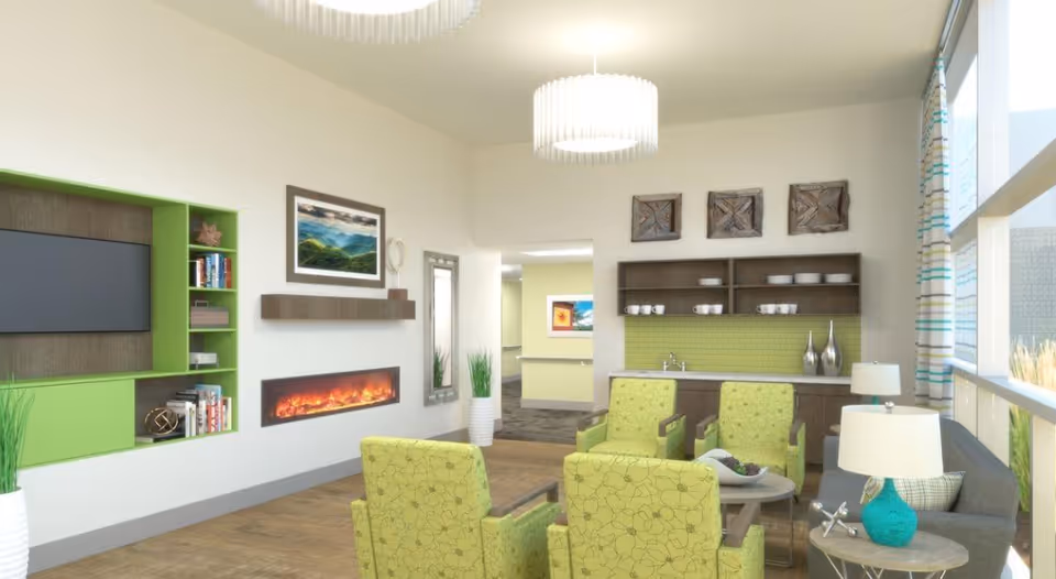 A bright and modern living room area with four green patterned armchairs arranged around a small round table, a gray sofa with a turquoise lamp on a side table, a wall-mounted electric fireplace below a landscape painting, built-in green shelving with books and decorative items, and a kitchenette with a sink and open shelves holding cups and bowls. Large windows with striped curtains let in natural light.