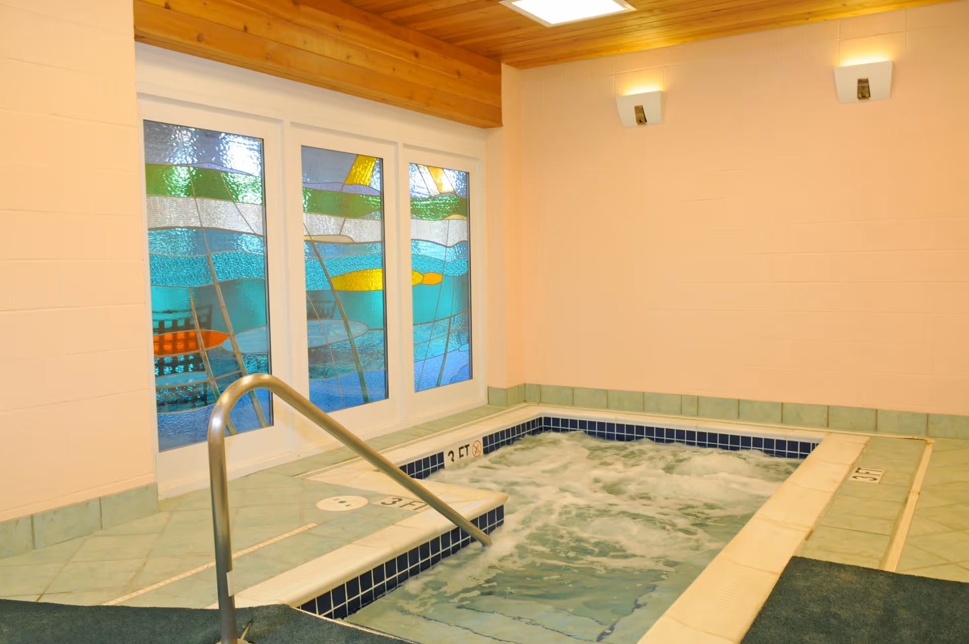 Small indoor hot tub with bubbling water, tiled surround and decorative stained-glass windows.