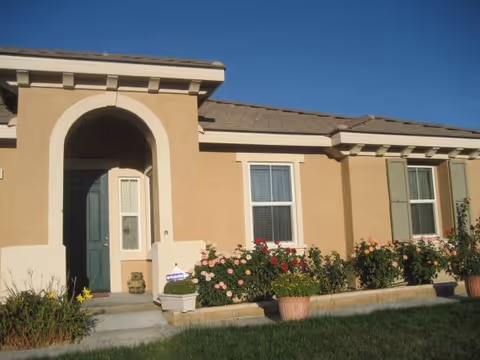 Exterior view of Alpine Care Assisted Living building with arched entrance and blooming plants.