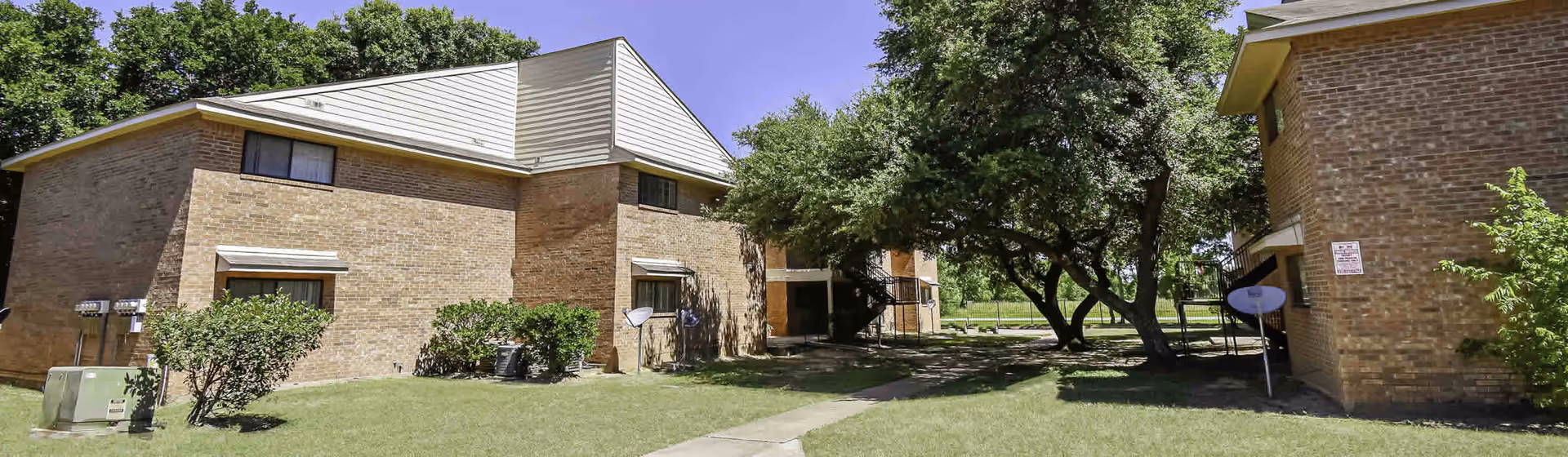 Exterior view of brick senior housing buildings with a grassy lawn, trees, and a walkway between structures.